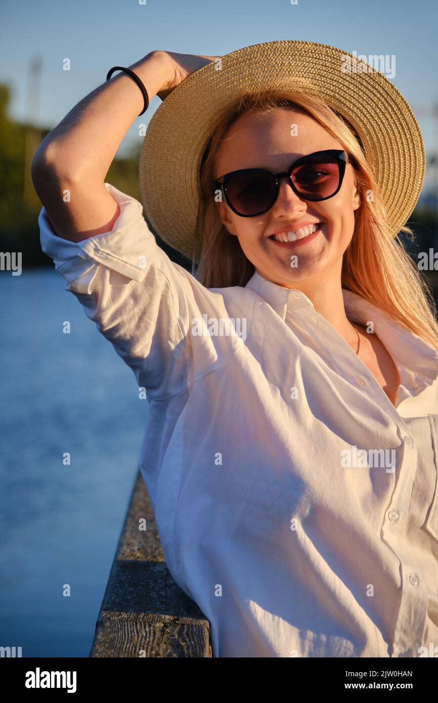 young happy blond woman in straw hat and sunglasses at summer sunset ...