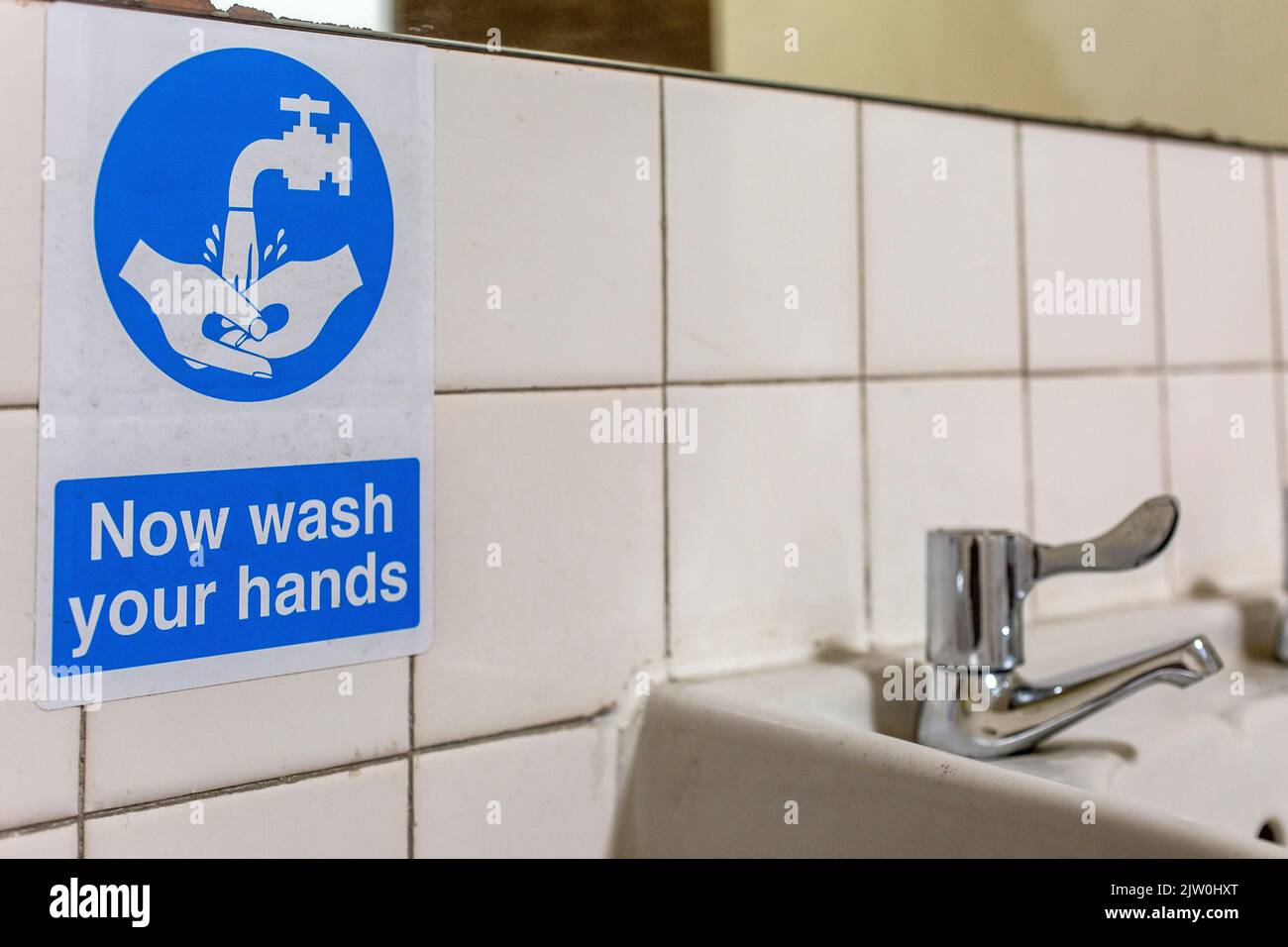 Wash your hands sign next to bathroom sink Stock Photo