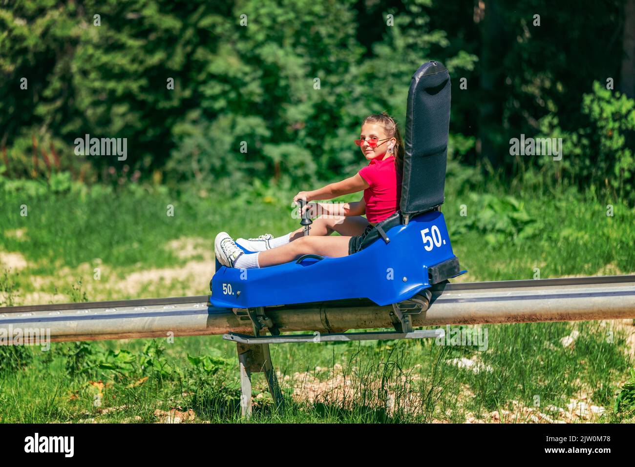 Girl go downhill ski slope on mountain roller coaster at summer. Summer tourism and fun on the mountain concept Stock Photo