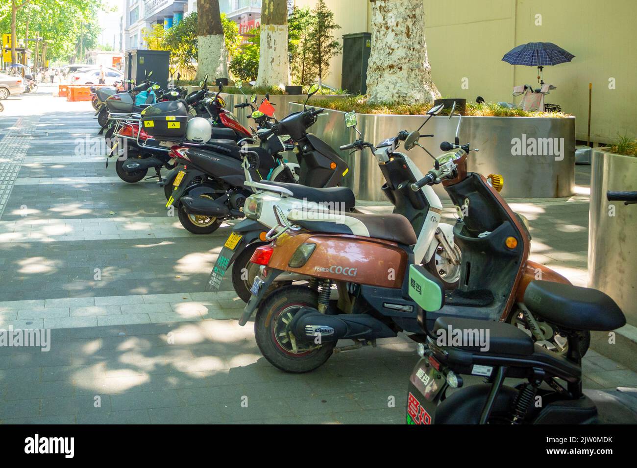 A variety of scooters or cycles are parked on a sidewalk in the