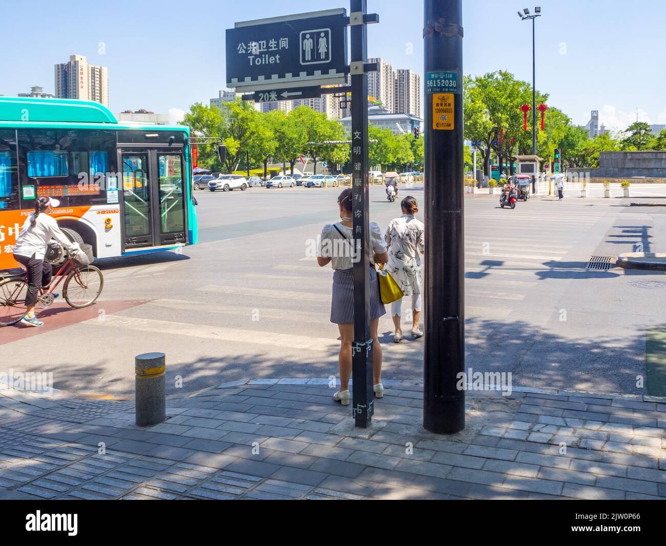 Chinese people cross a downtown district avenue using a crosswalk. A bus and a person on a