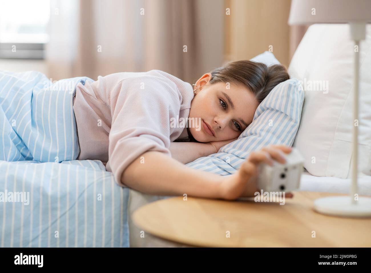 girl looking at alarm clock in bed in morning Stock Photo Alamy