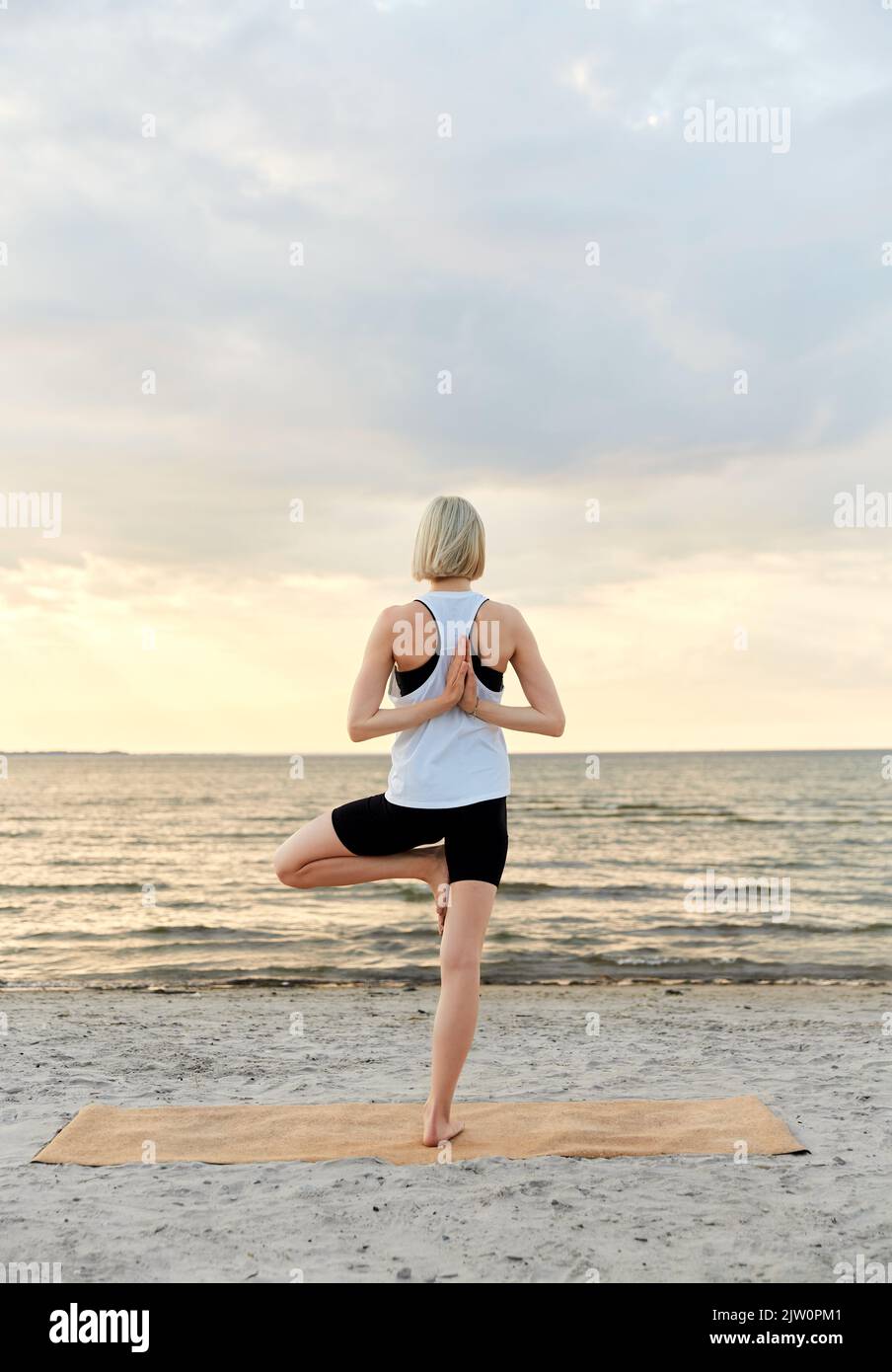 woman doing yoga tree pose on beach over sunset Stock Photo - Alamy