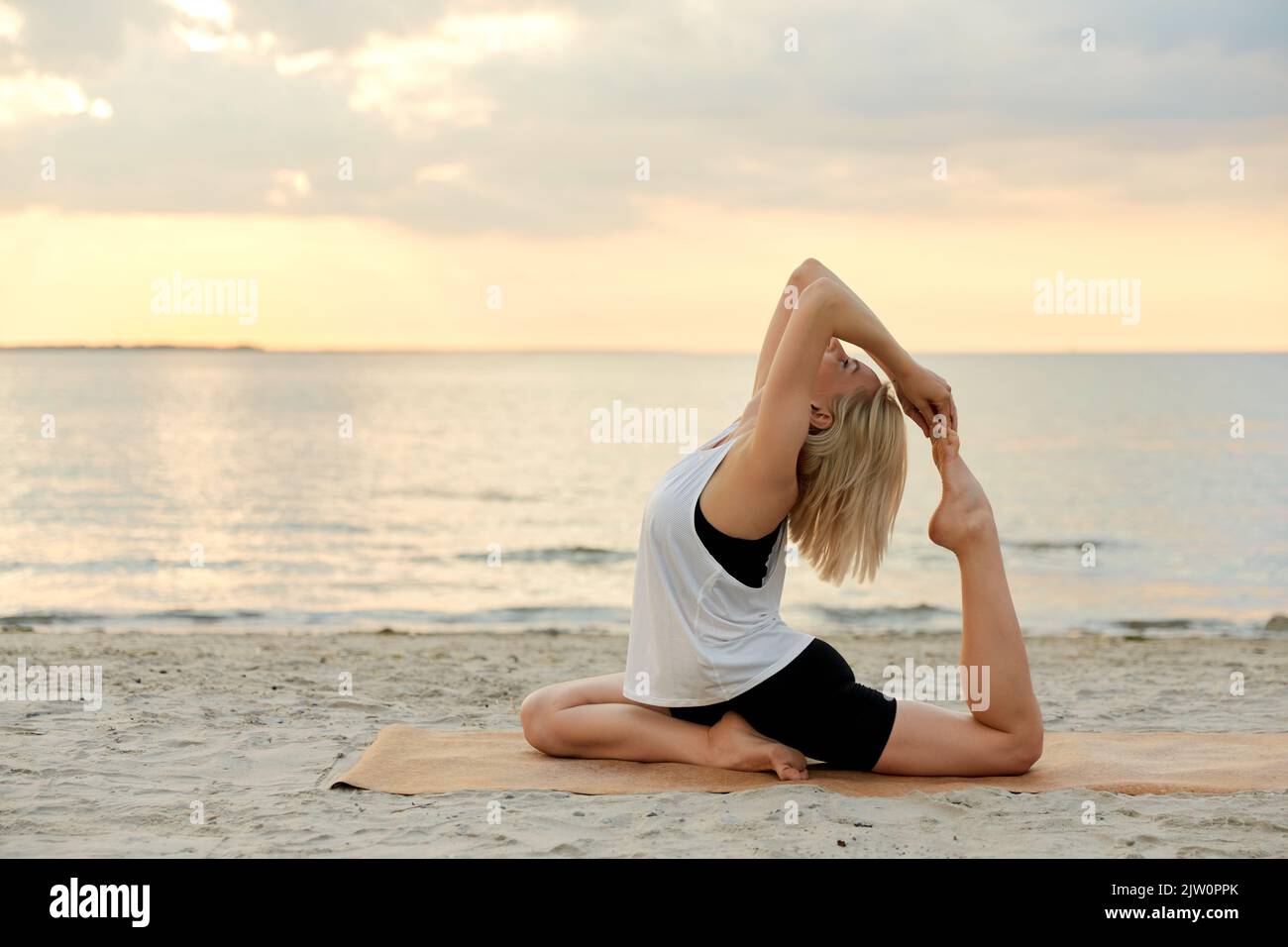 woman-doing-yoga-pigeon-pose-on-beach-2JW0PPK.jpg