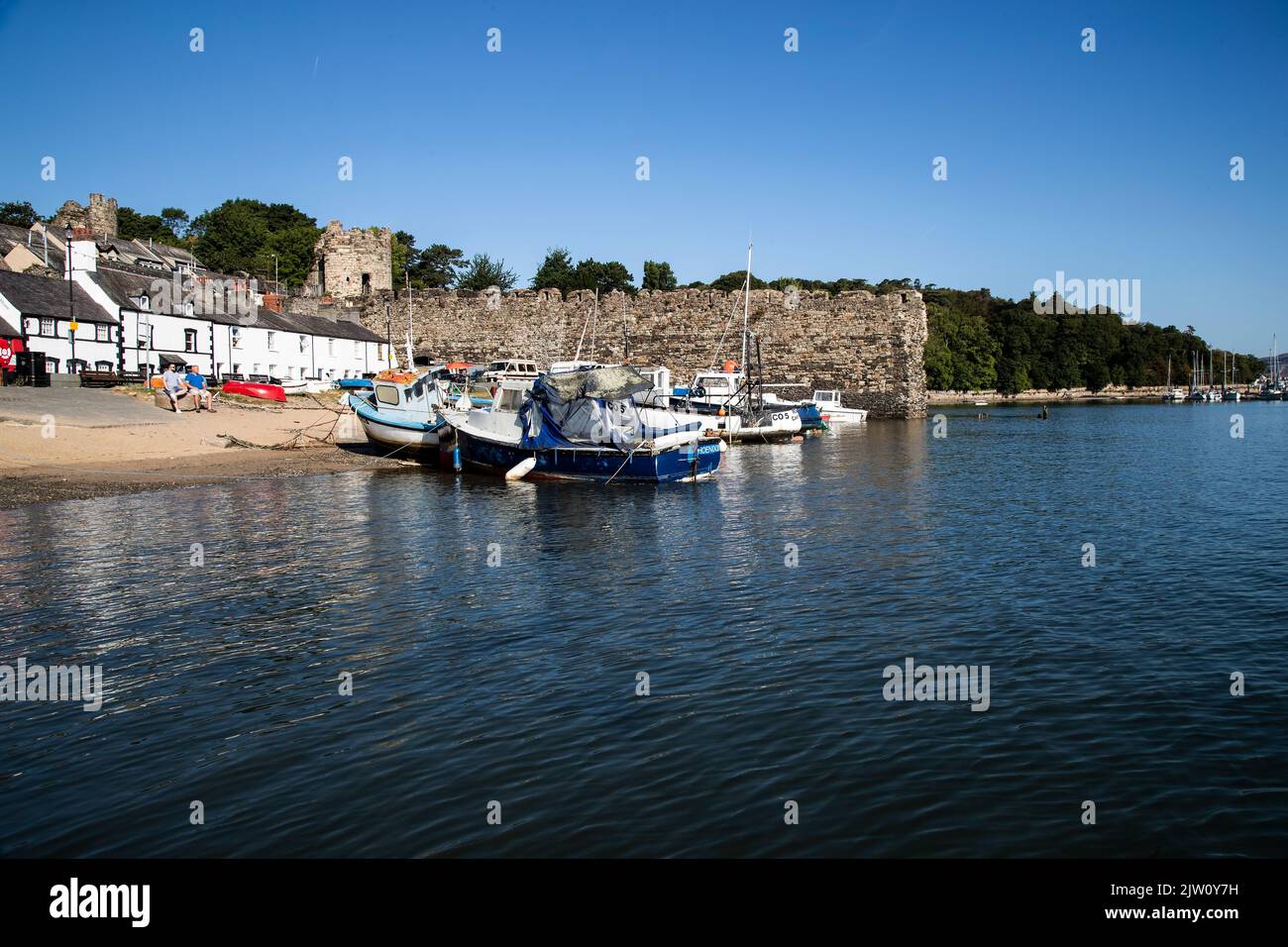 Small fishing boats hauled up on the foreshore at Conwy quayside, North Wales on a calm summer morning with the spur wall of the town beyond Stock Photo