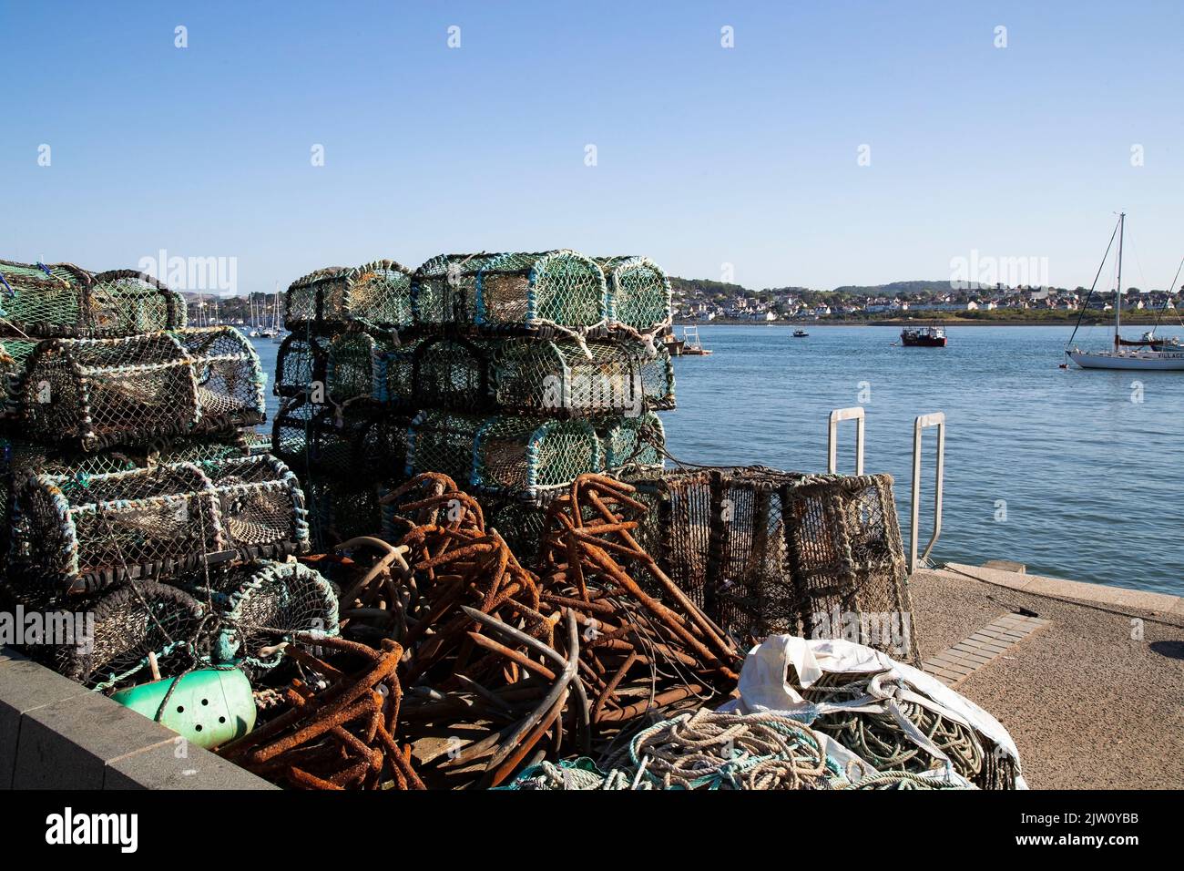 Lobster Pots, fishing tackle, ropes and lines stacked on the quayside at Conwy harbour adjacent to the fishing vessels on a summer dawn in North Wales Stock Photo