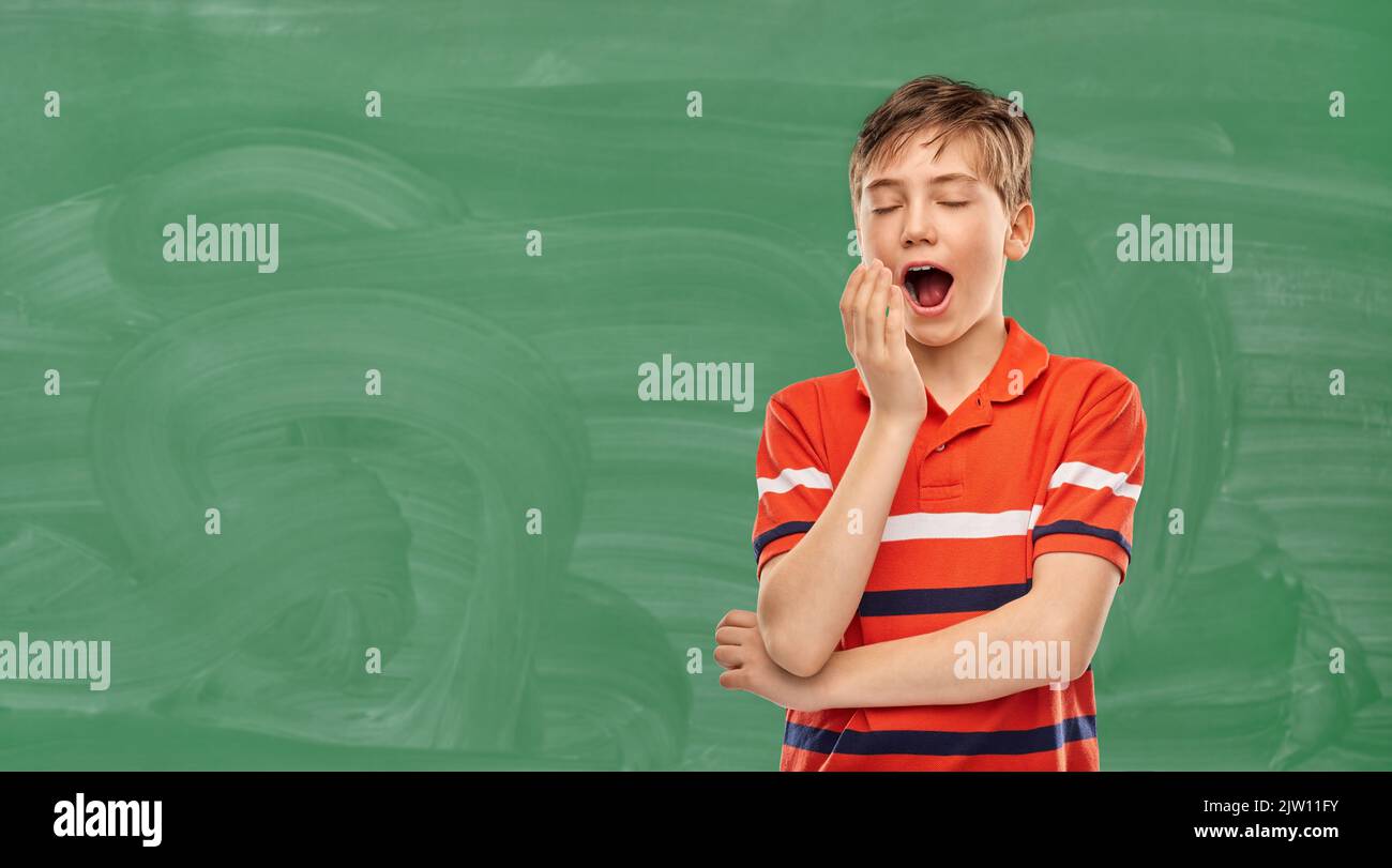 tired yawning student boy over green chalkboard Stock Photo