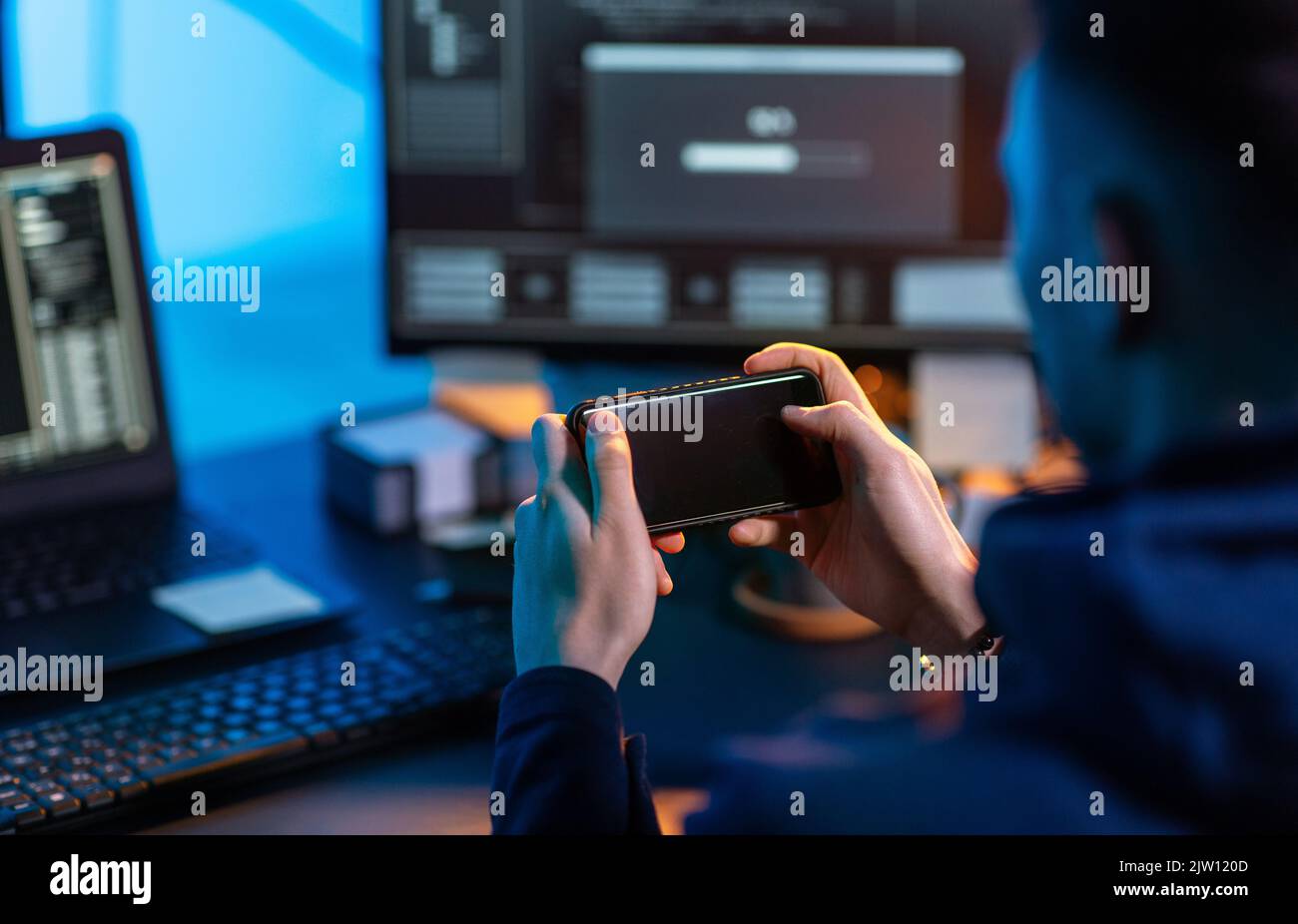 hacker with smartphone and computers in dark room Stock Photo