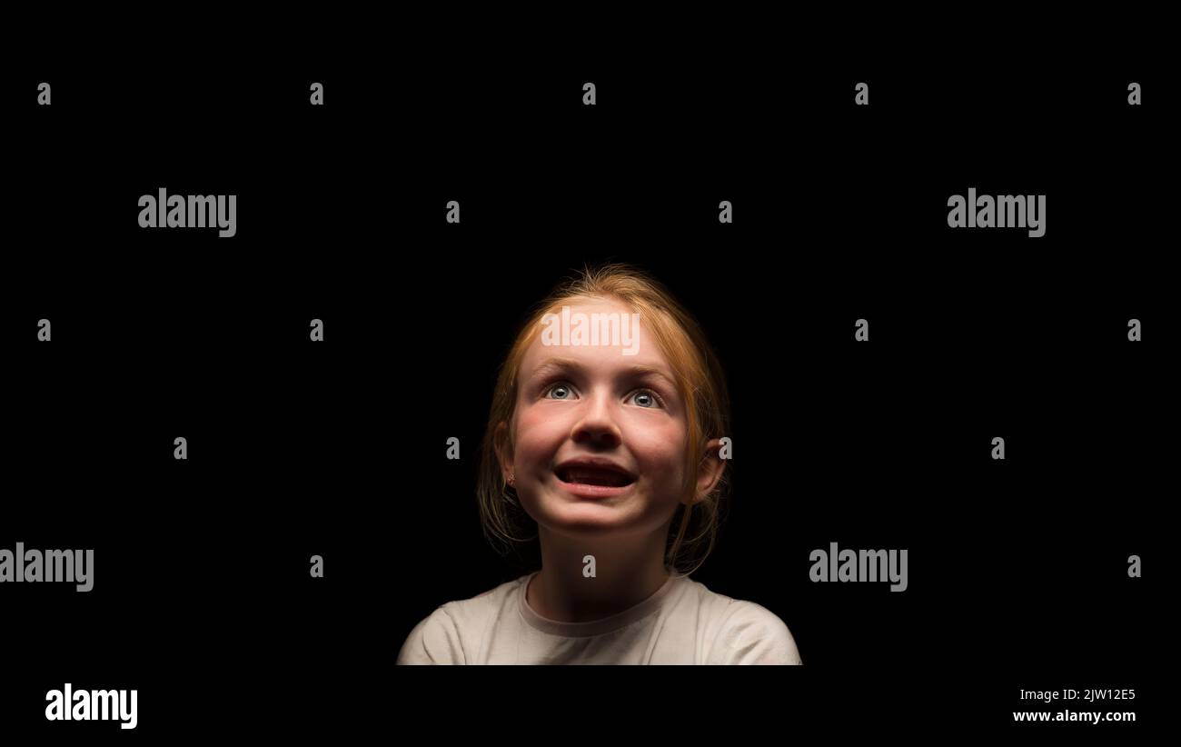 Young Caucasian female with a happy expression looking upwards in a dark environment. Stock Photo