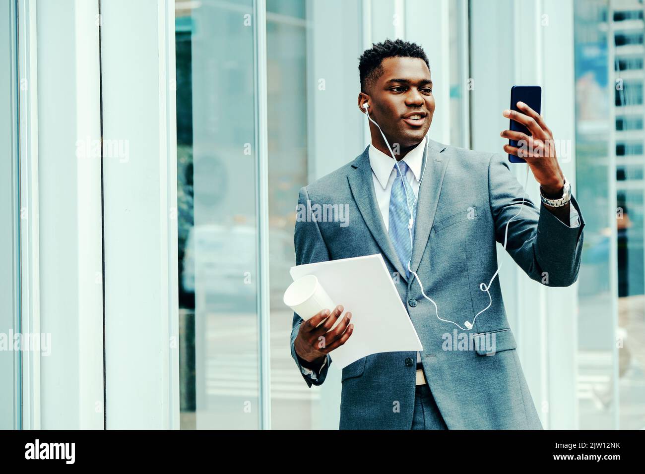 Positive young entrepreneur using smartphone outside wearing suit and tie Stock Photo