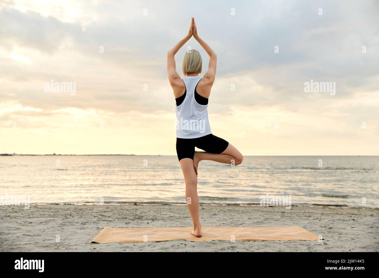 woman doing yoga tree pose on beach over sunset Stock Photo - Alamy