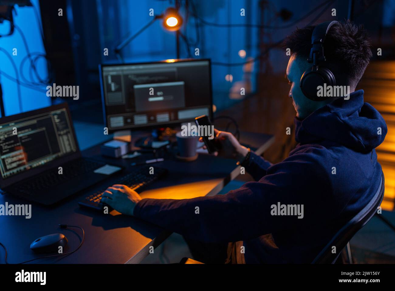 hacker with smartphone and computers in dark room Stock Photo