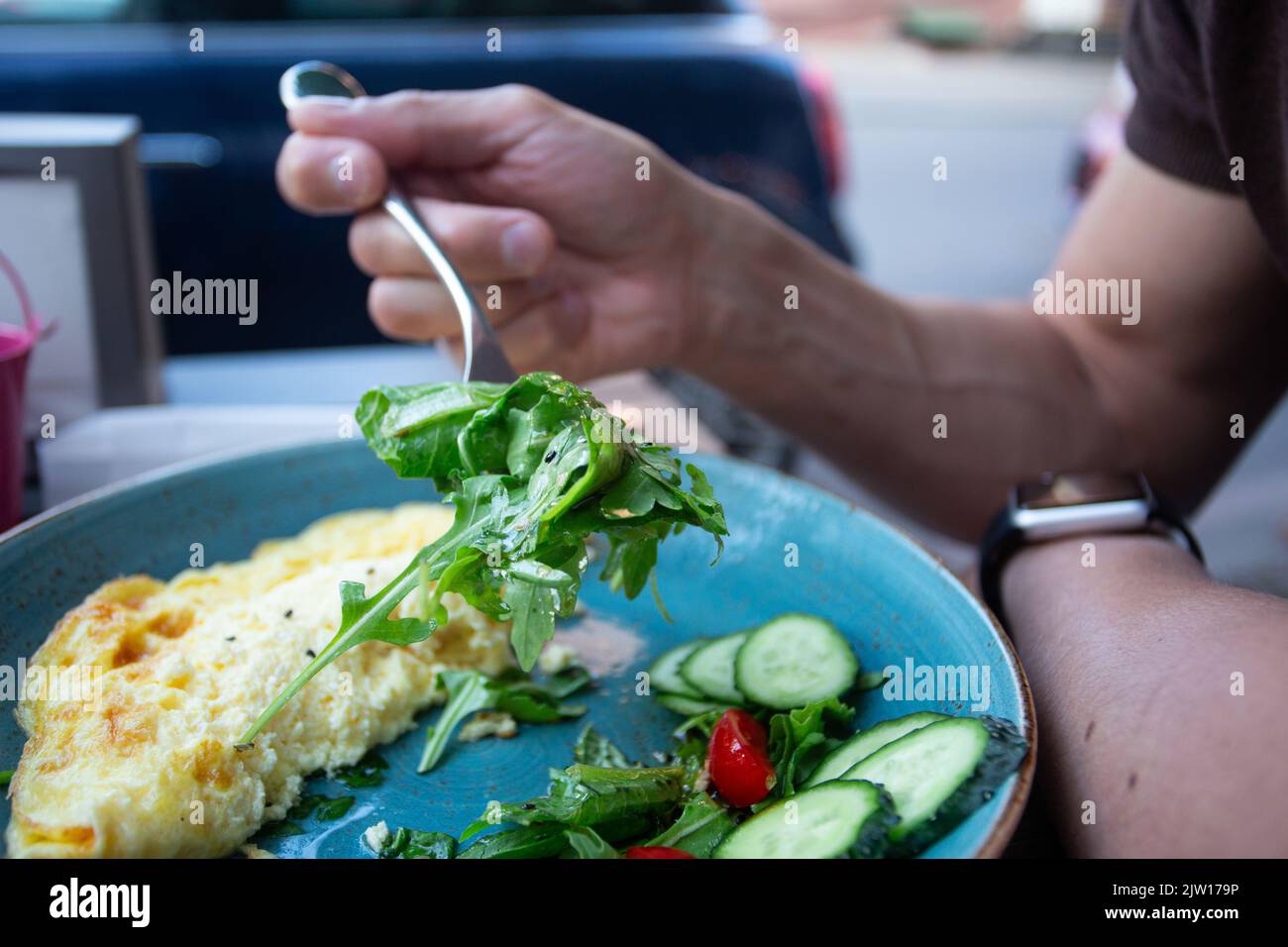 Fit young man enjoys healthy breakfast, scrambled egg with green vegetables and t tomatos Stock Photo