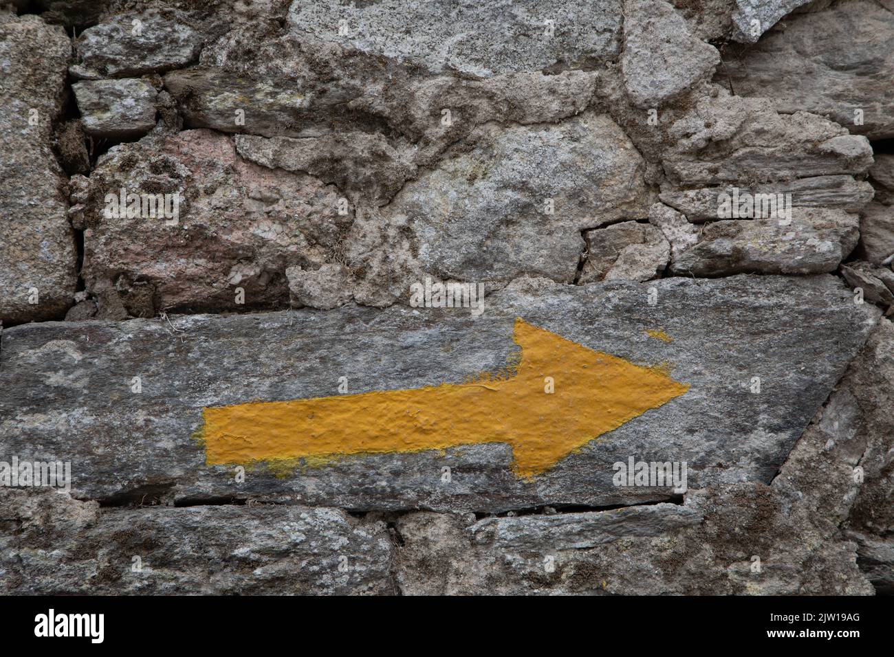 Yellow Arrow on a stone wall, Camino to Santiago de Compostela, Spain Stock Photo