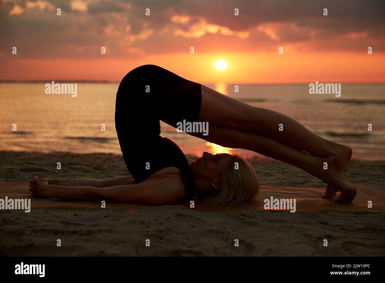woman doing yoga plow pose on beach Stock Photo