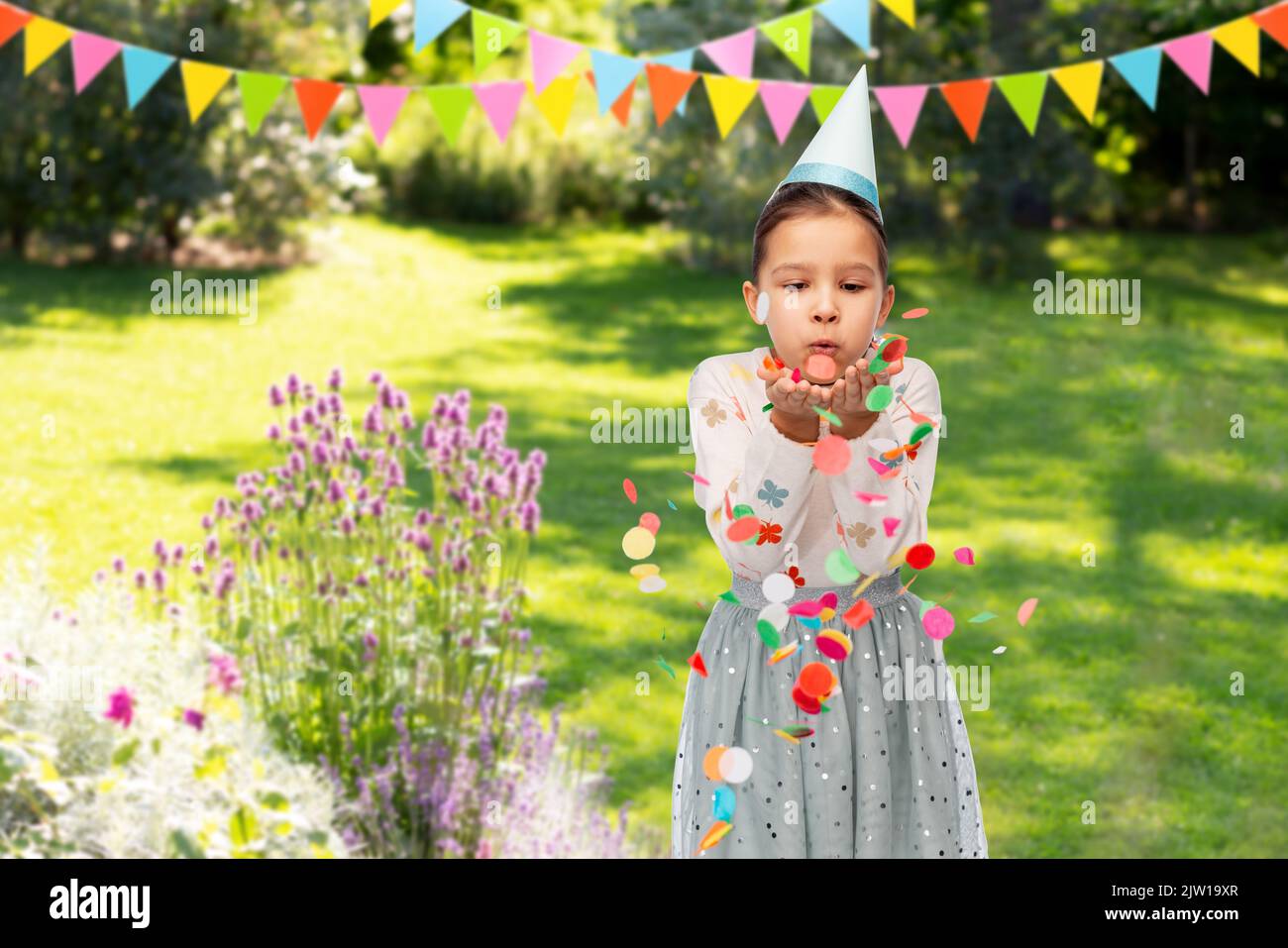 girl blowing confetti at birthday party in garden Stock Photo