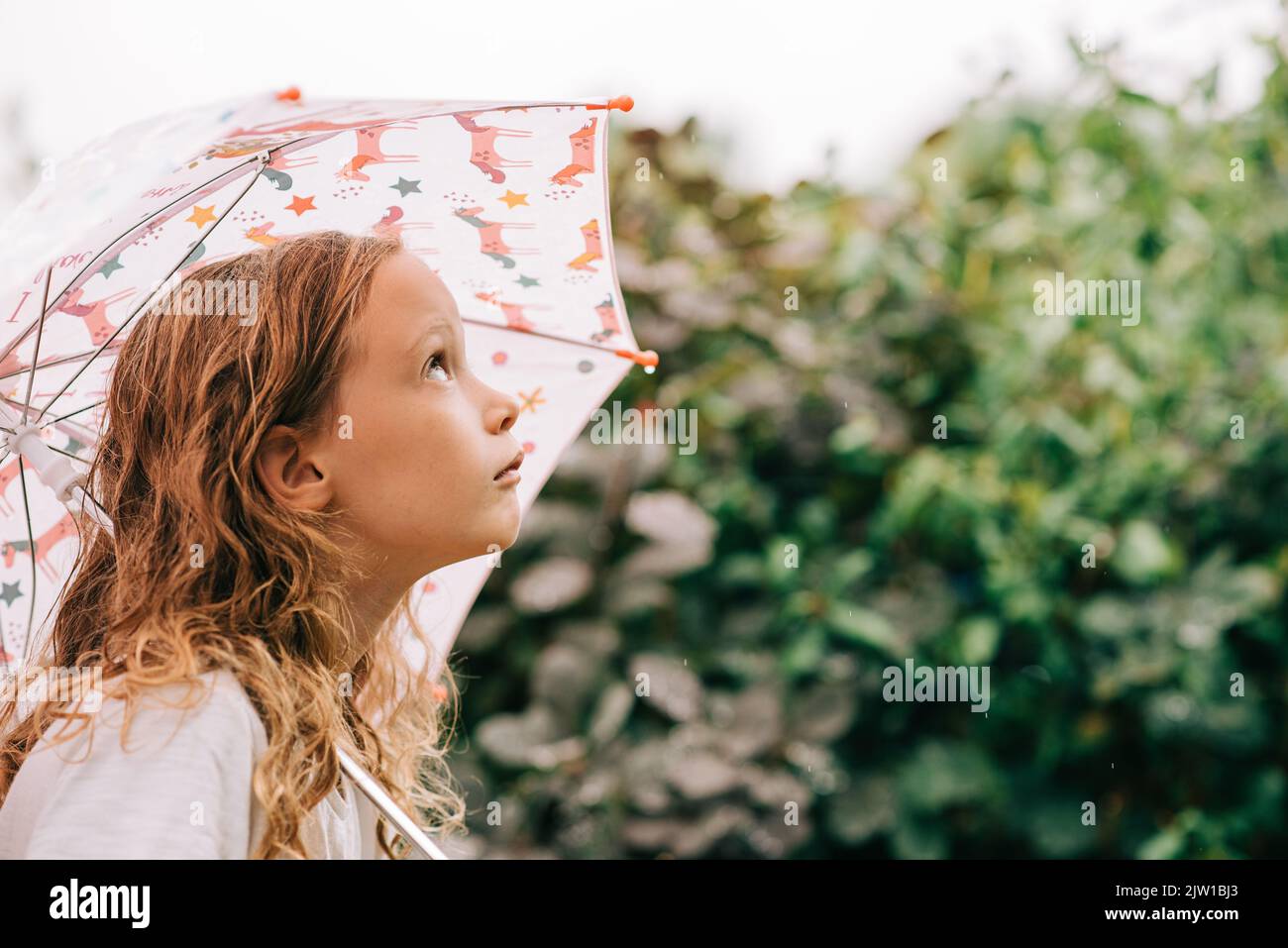 child holding an umbrella looking up at the sky at the rain Stock Photo