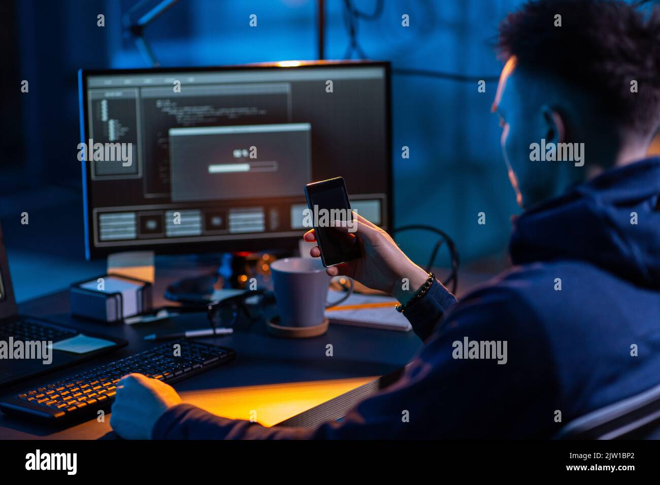 hacker with smartphone and computers in dark room Stock Photo