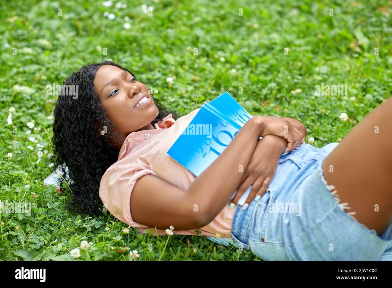 african student girl with textbook lying on grass Stock Photo - Alamy