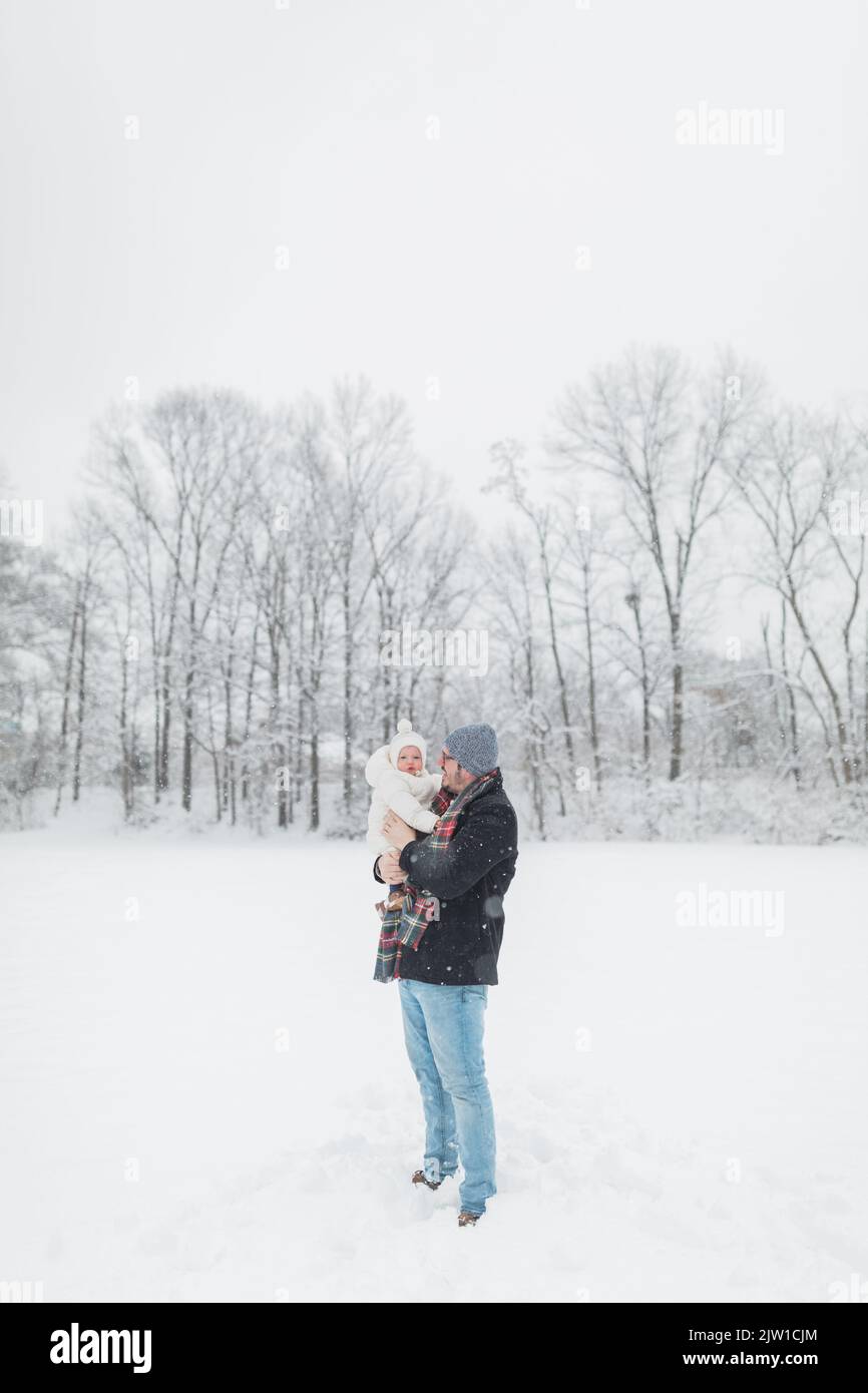 30-year-old father holds up 12-month-old baby in snowy field. Stock Photo