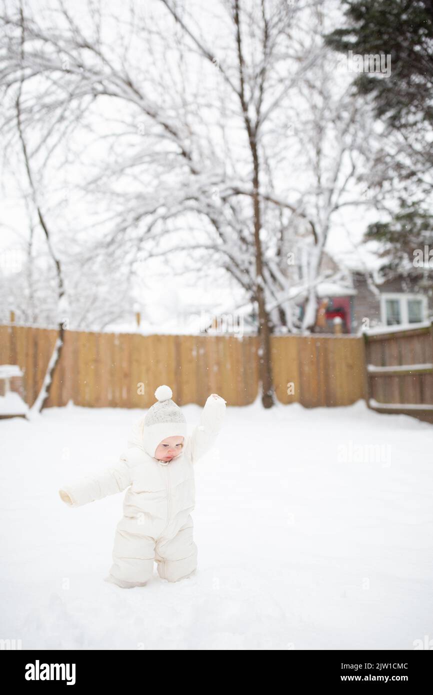 12-month-old Caucasian baby boy in snow suit throws snow in air. Stock Photo