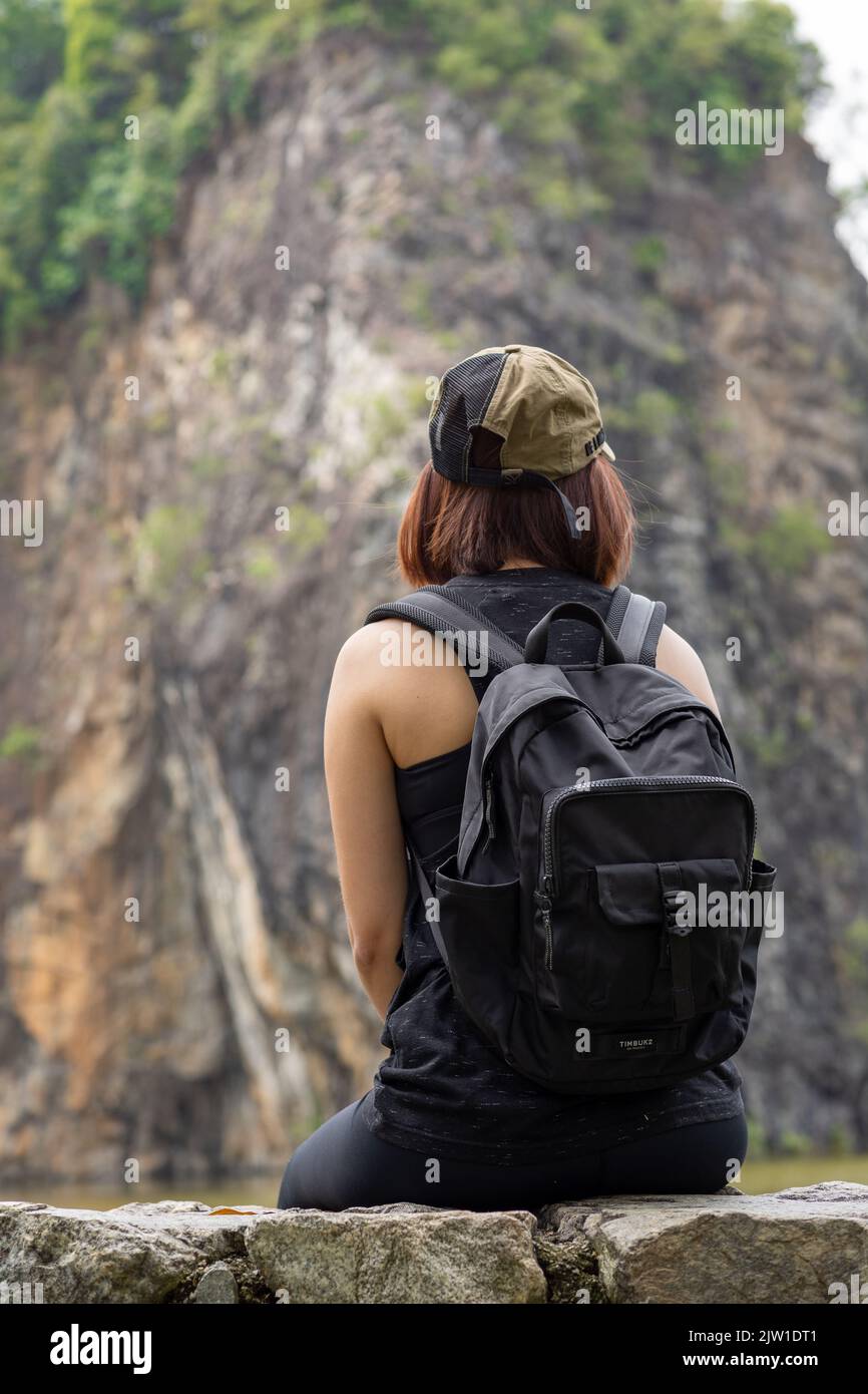 A rear view of a female looking the cliff view while sitting on a rock ...