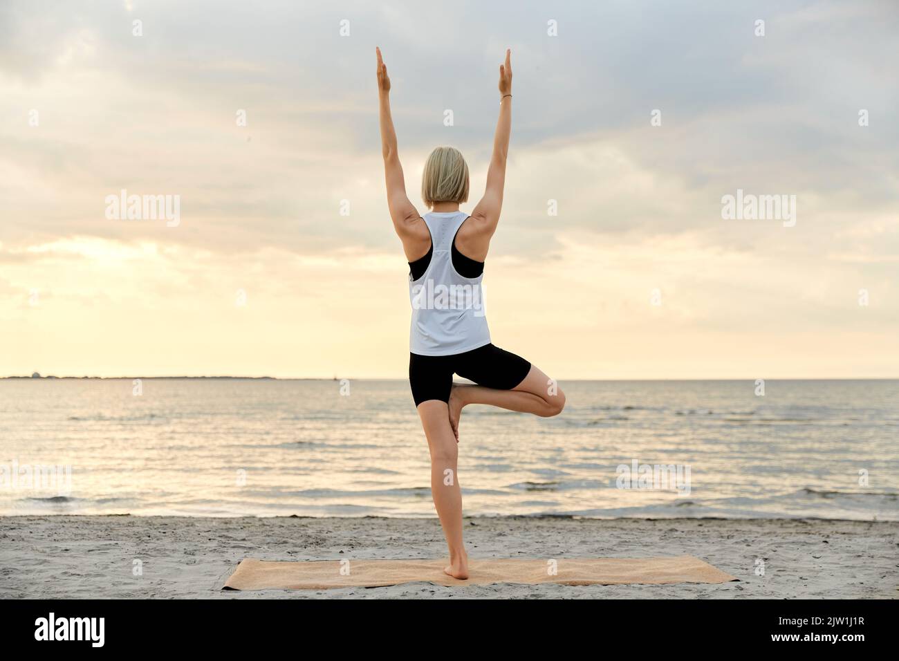 woman doing yoga tree pose on beach over sunset Stock Photo - Alamy