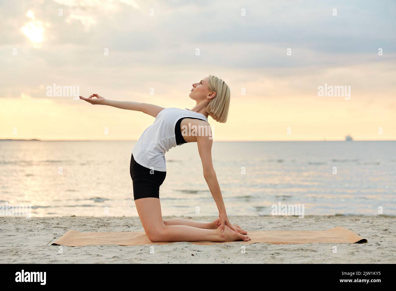 woman doing yoga camel pose on beach Stock Photo