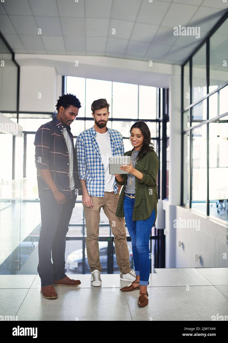 Getting creative together. three young designers working on a digital tablet in a modern office. Stock Photo