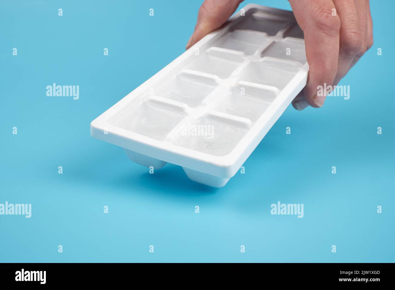 box with ice cubes in hand on a blue background. Stock Photo