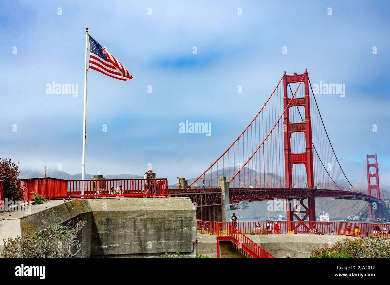 The Star Spangled Banner flag flies on a flagpole in the foreground with The Golden Gate Bridge in the background Stock Photo