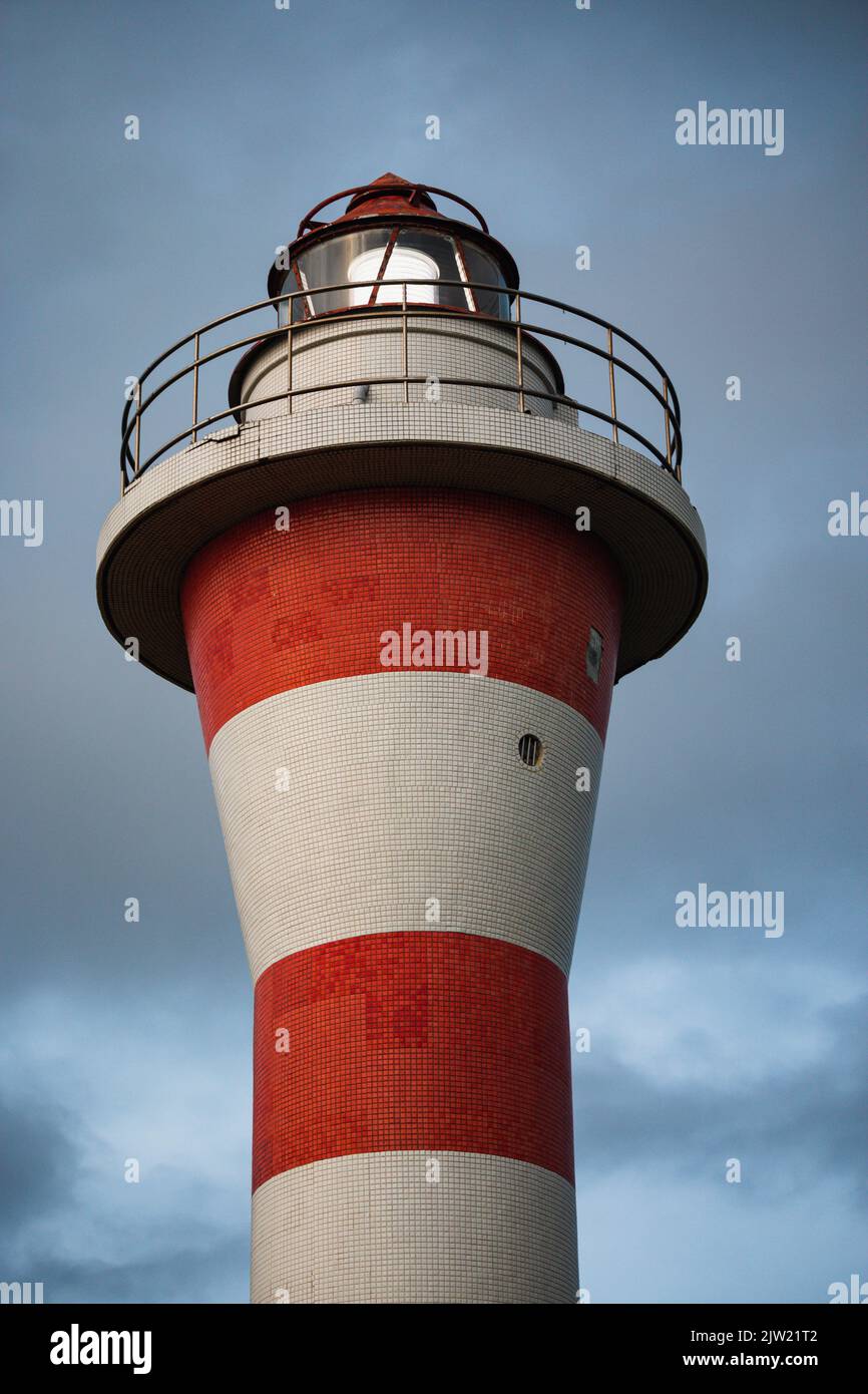 Red and white striped lighthouse against dark storm clouds Stock Photo