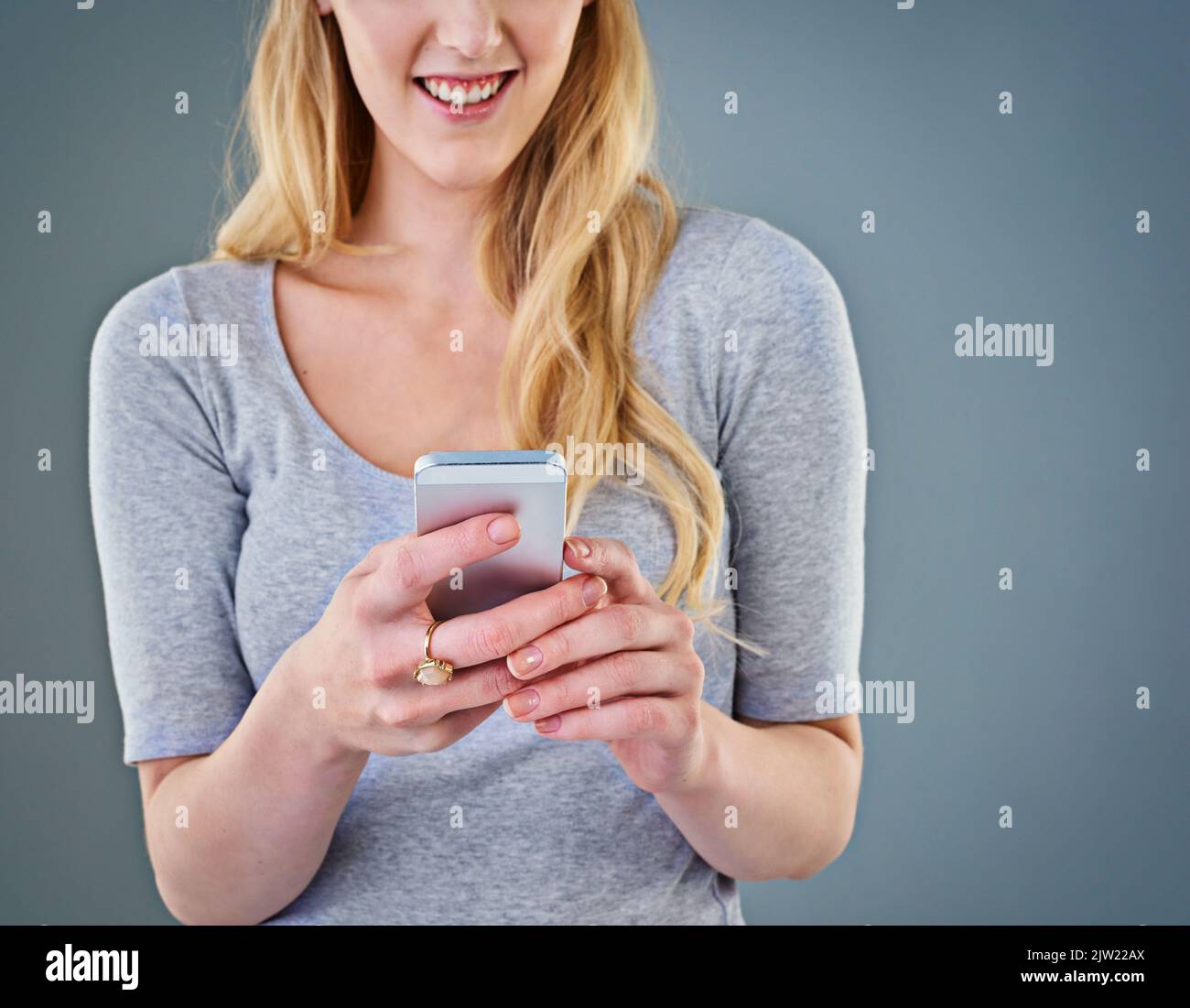 Lemme just reply to this text. Cropped studio shot of a young woman looking at her smartphone. Stock Photo