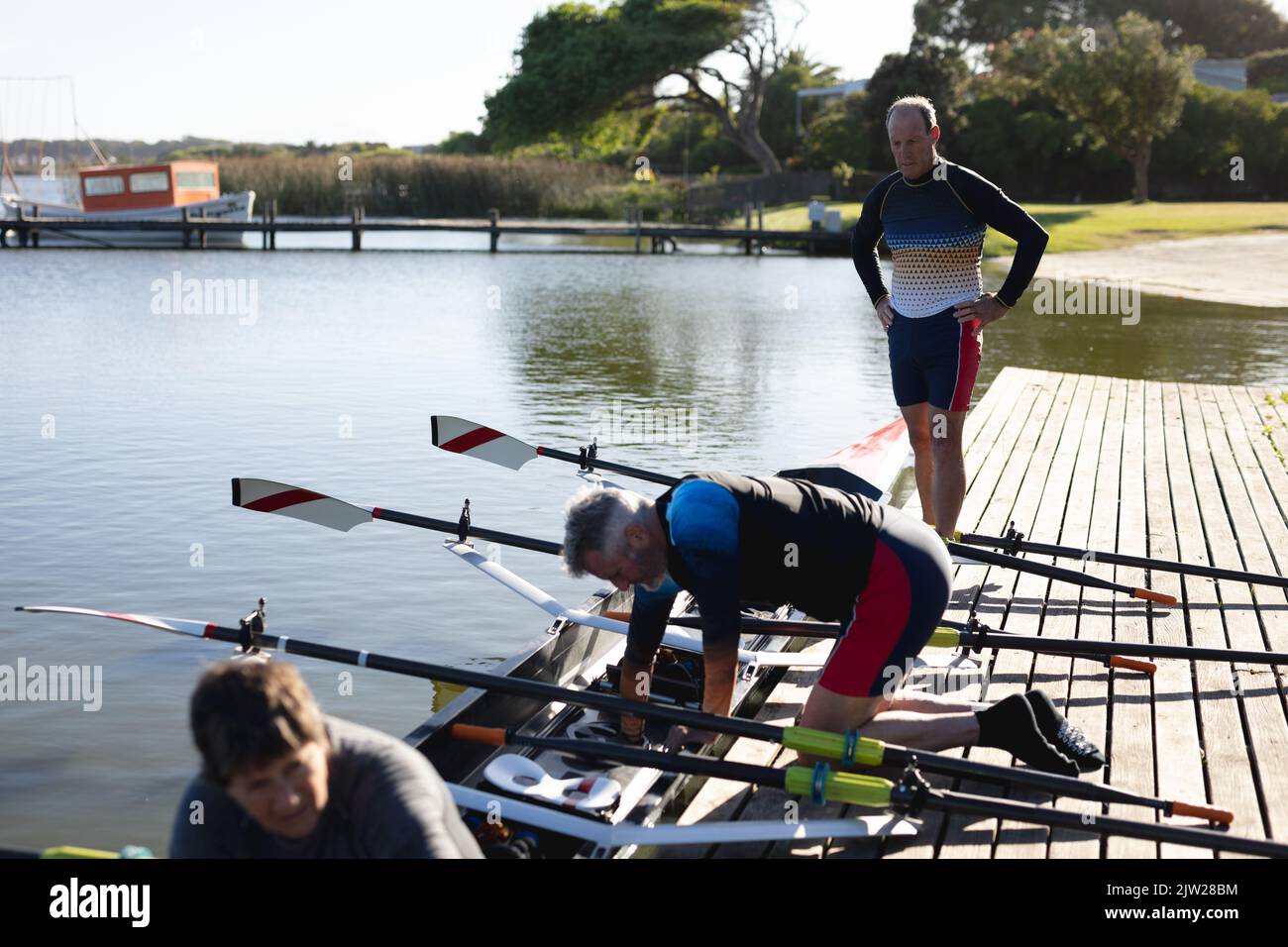 Senior caucasian rowing team attaching oars to the boat near the wooden dock Stock Photo