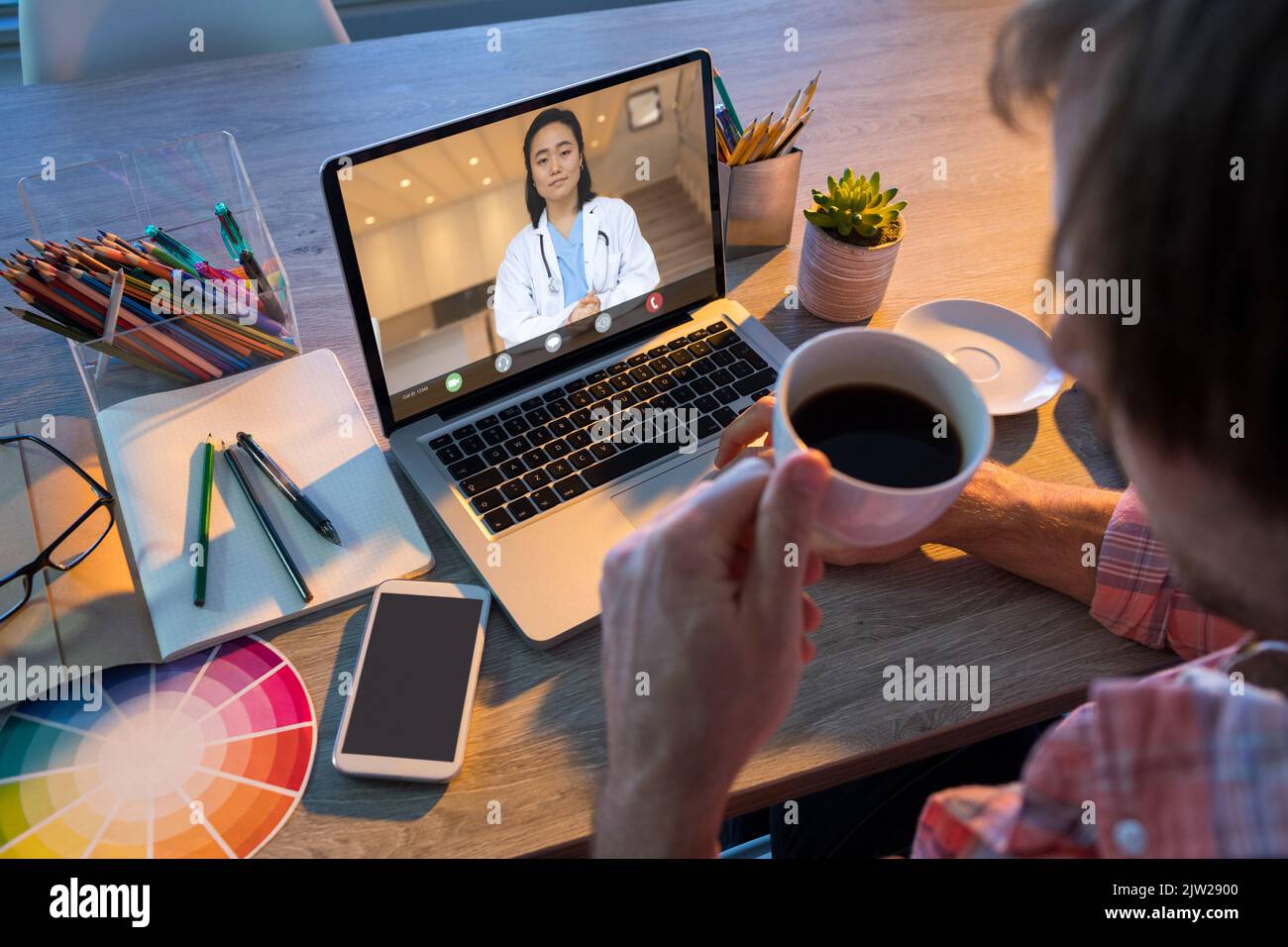 Caucasian businessman having coffee during video conference with asian female doctor Stock Photo