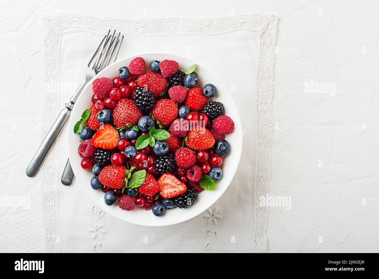 Bowl of healthy fresh berry fruit meal on white table background. Top view. Berries overhead closeup colorful assorted mix of strawberry, blueberry, r Stock Photo