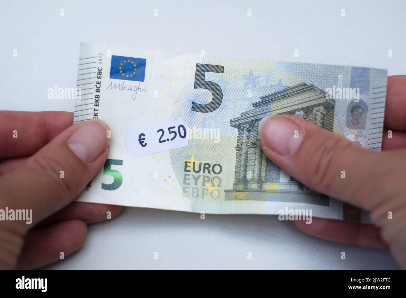 Five euro banknote with 2 euro 5 cent price tag. Selective focus on label. Inflation in Europe, hyper inflation, devaluation of fiat money concept. Stock Photo