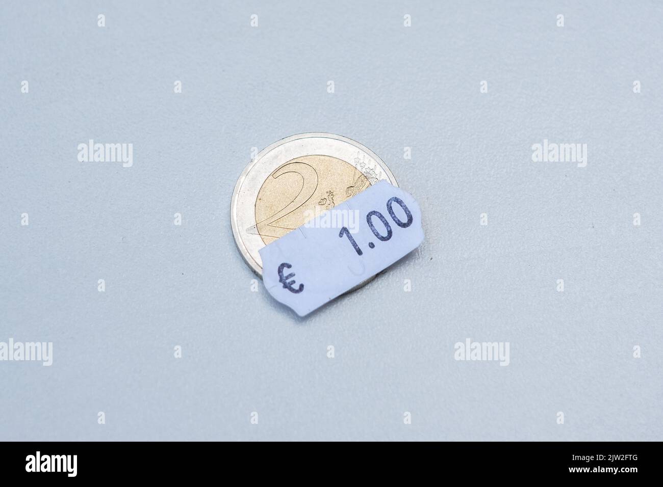 Two euro coin with one euro price tag. Selective focus on label. Inflation in Europe, hyper inflation, devaluation of fiat money concept. Stock Photo
