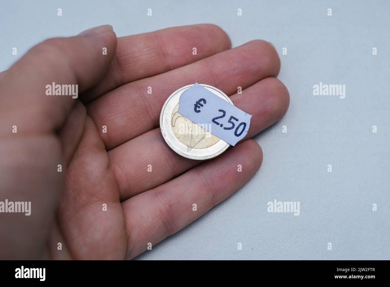 Hand holding two euro coin with 2 euro 5 cent price tag. Selective focus on label. Inflation in Europe, hyper inflation. Stock Photo
