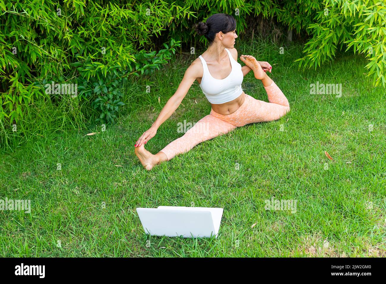 From above full body of active female practicing Eka Pada Raja Kapotasana D posture during online yoga training in park Stock Photo
