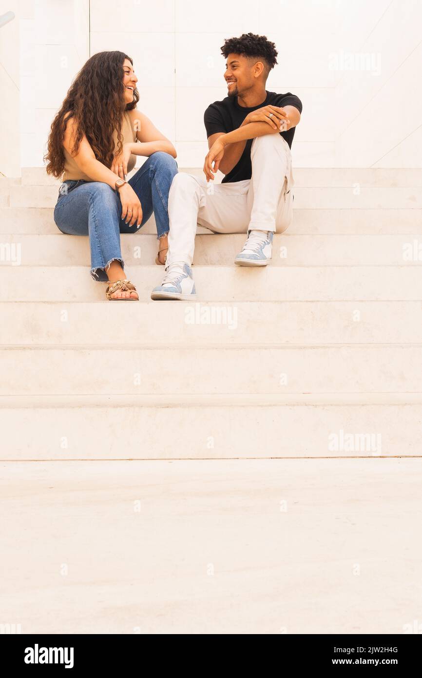 Full length of smiling young couple talking while sitting on steps Stock Photo