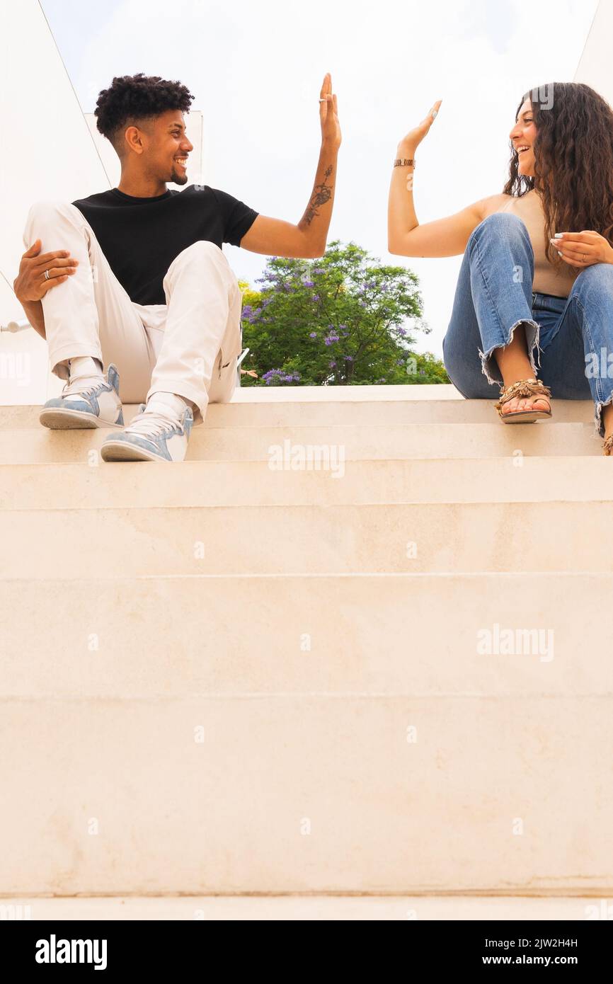 Smiling young couple doing high-five while sitting on steps Stock Photo