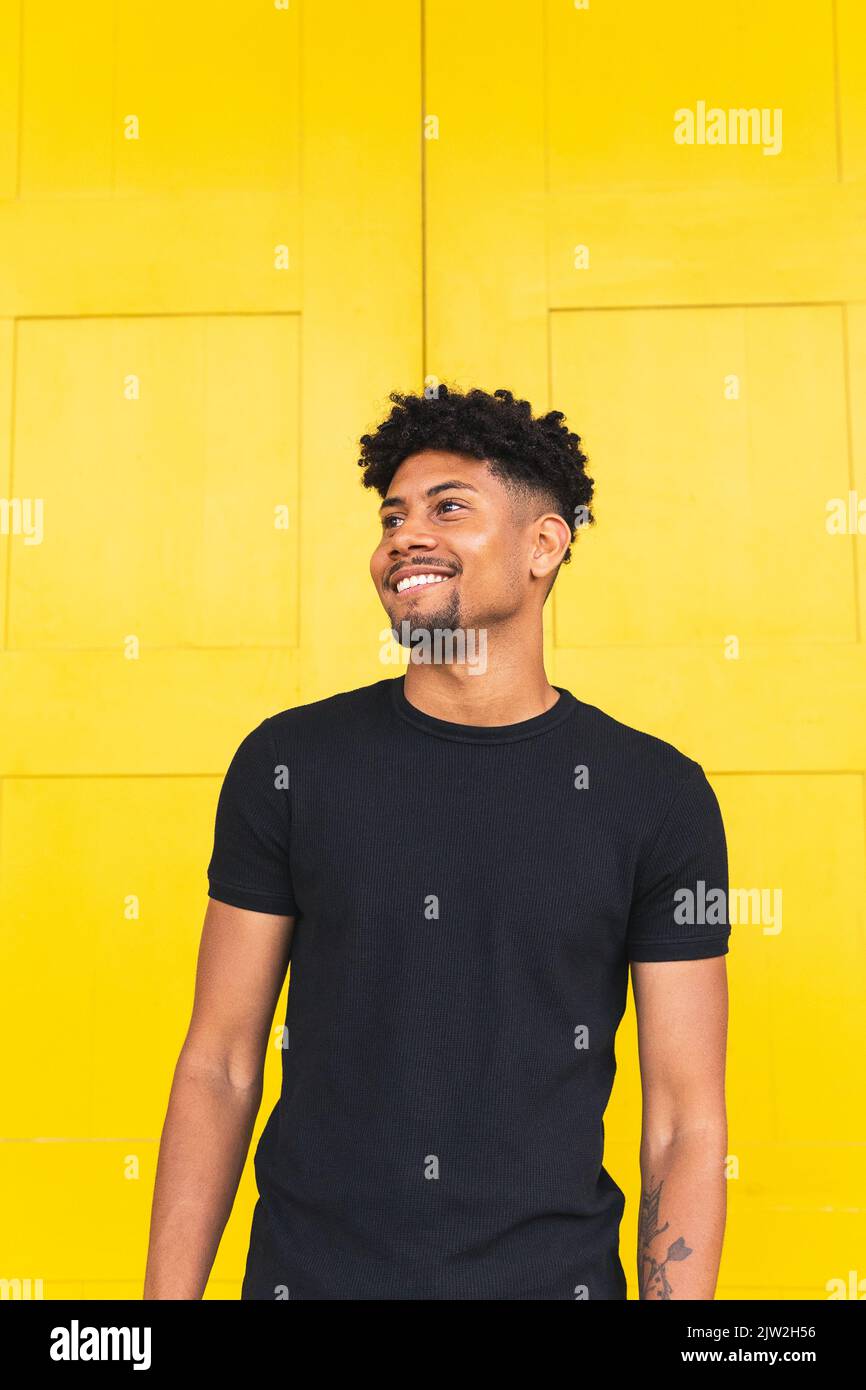 Happy young man looking away while standing against yellow wall Stock Photo