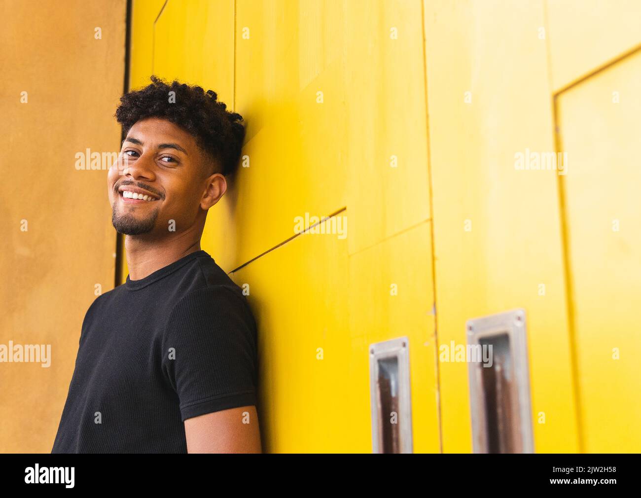 Happy young man looking at camera while standing against yellow wall Stock Photo