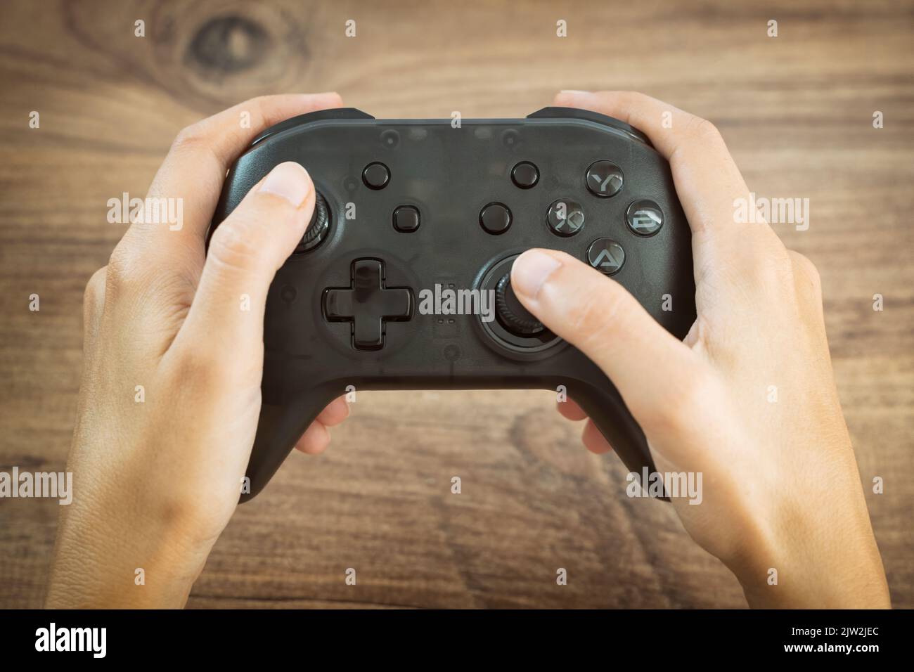 Hands Holding Black Wireless Gamepad On Top Of A Wooden Surface Stock Photo