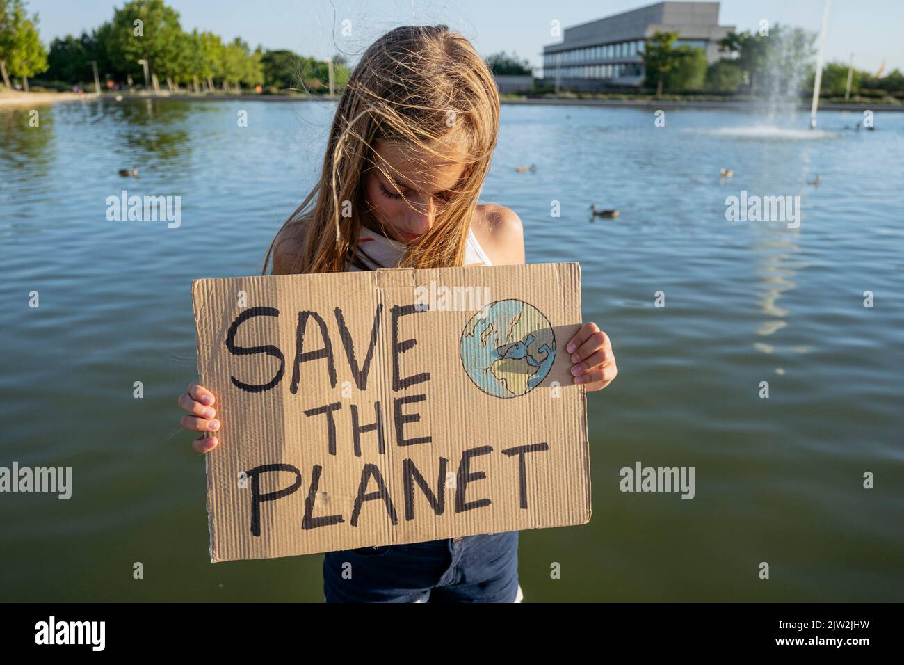Teenage girl holding cardboard poster with Save The Planet inscription standing near river on street on summer day in coastal area Stock Photo