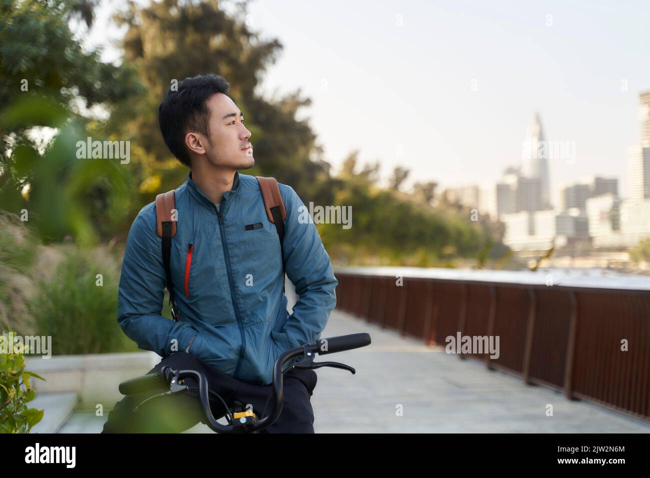 asian young adult man sitting on bicycle looking at view in city park Stock Photo