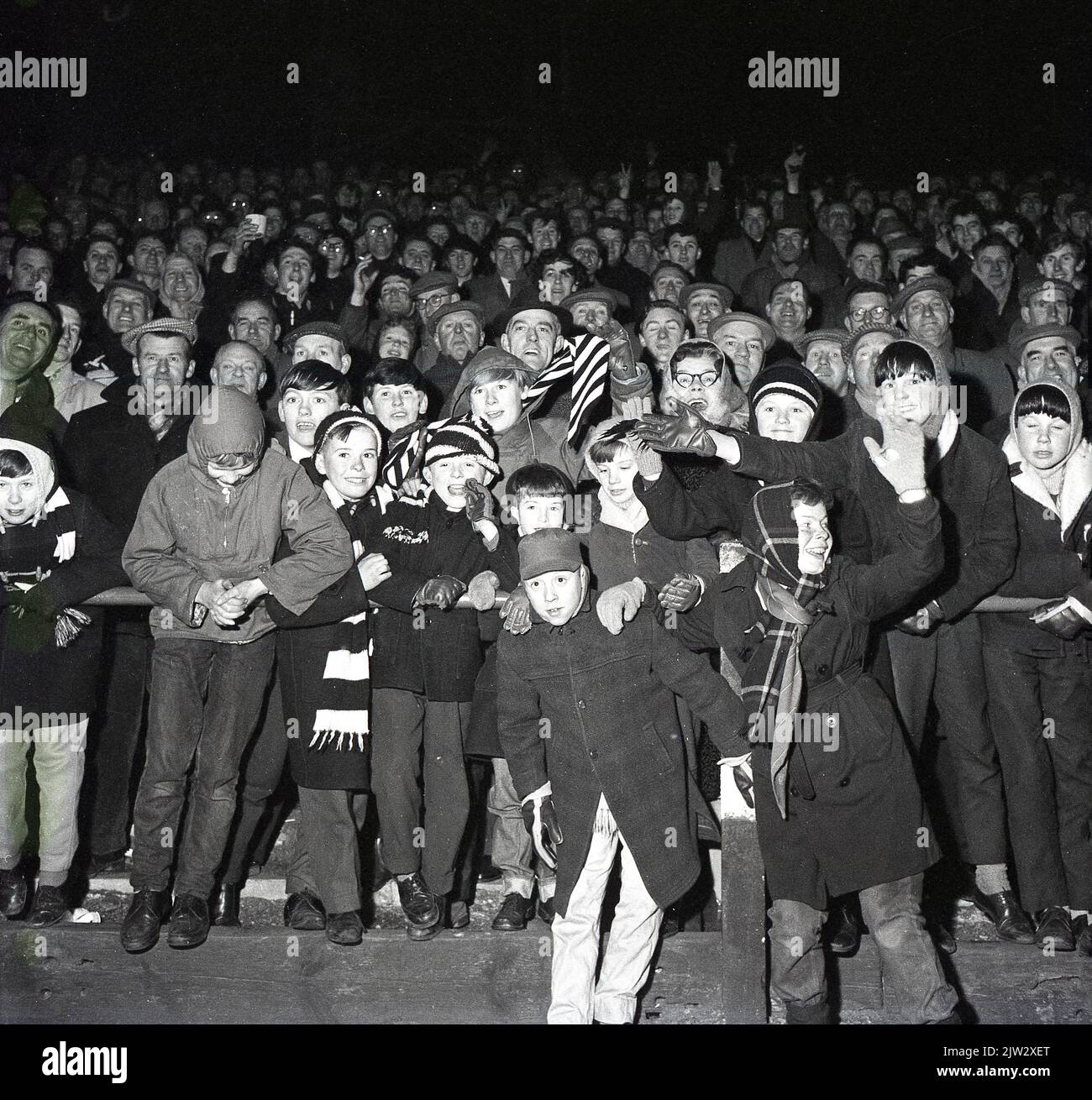 1960s, historical, football fans, evening match, coats, flat caps for the men, duffel coats and bobble hats for the youngsters, not a replica shirt in sight! Stock Photo
