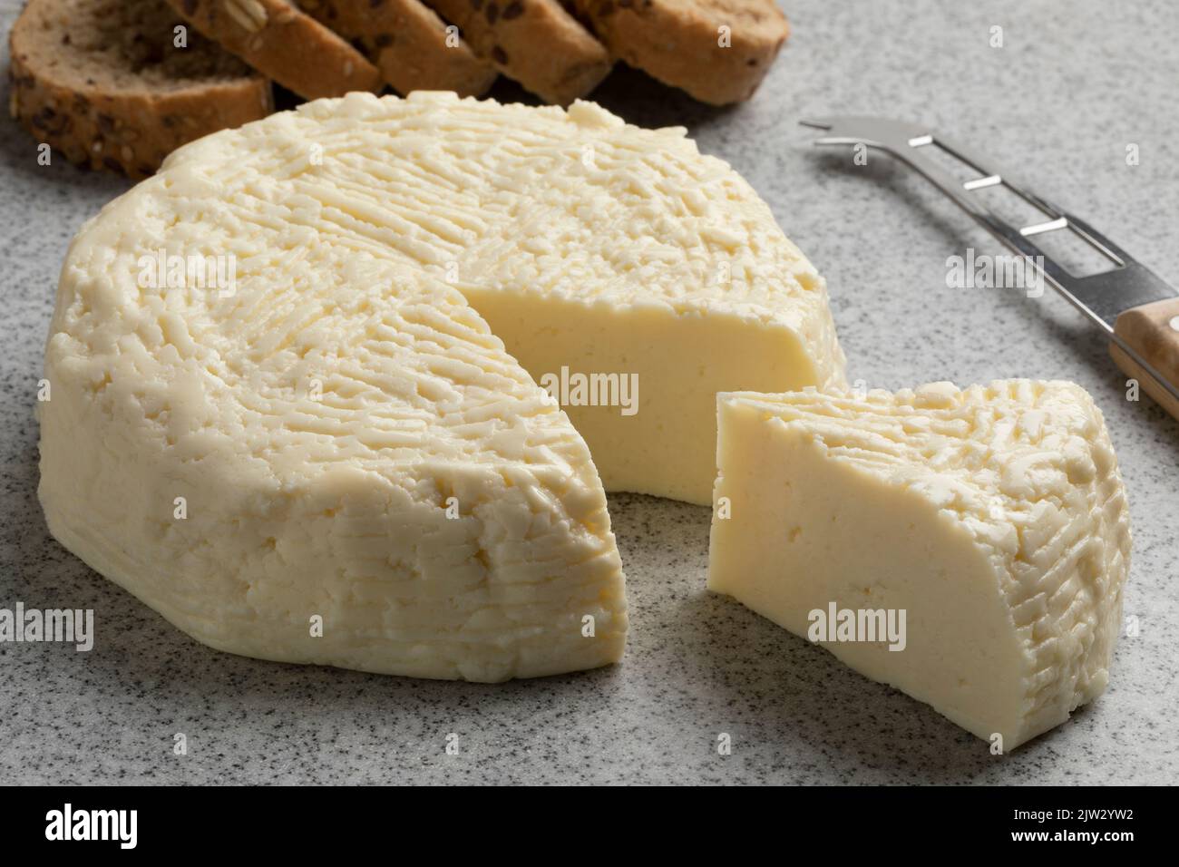 Piece of traditional Croatian homemade white cheese of cooked milk, Kuhani sirevi, on a cutting board close up Stock Photo