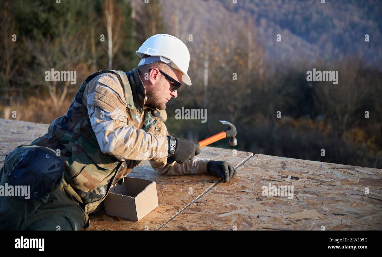 Carpenter hammering nail into OSB panel on the roof top of future